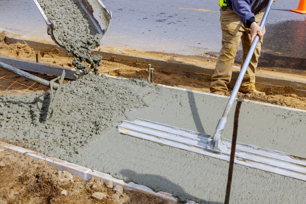 Construction worker pour cement for sidewalk in concrete works with mixer truck with wheelbarrow at